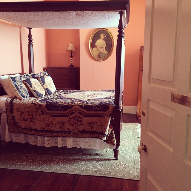 A haunted bedroom, with canopy bed and portrait on the wall.